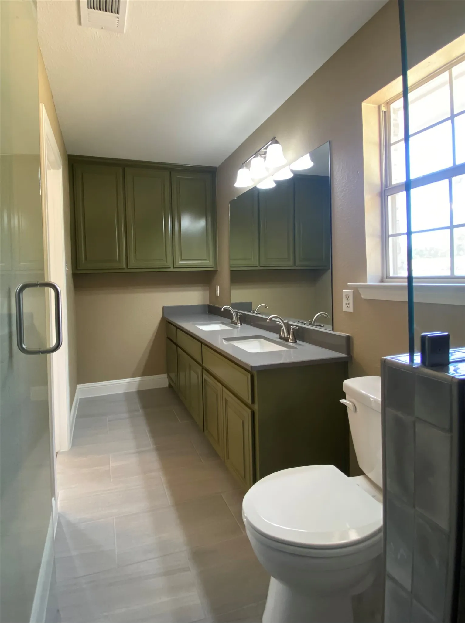 Double vanity featuring dual sinks, overhead cabinetry, and a large mirror