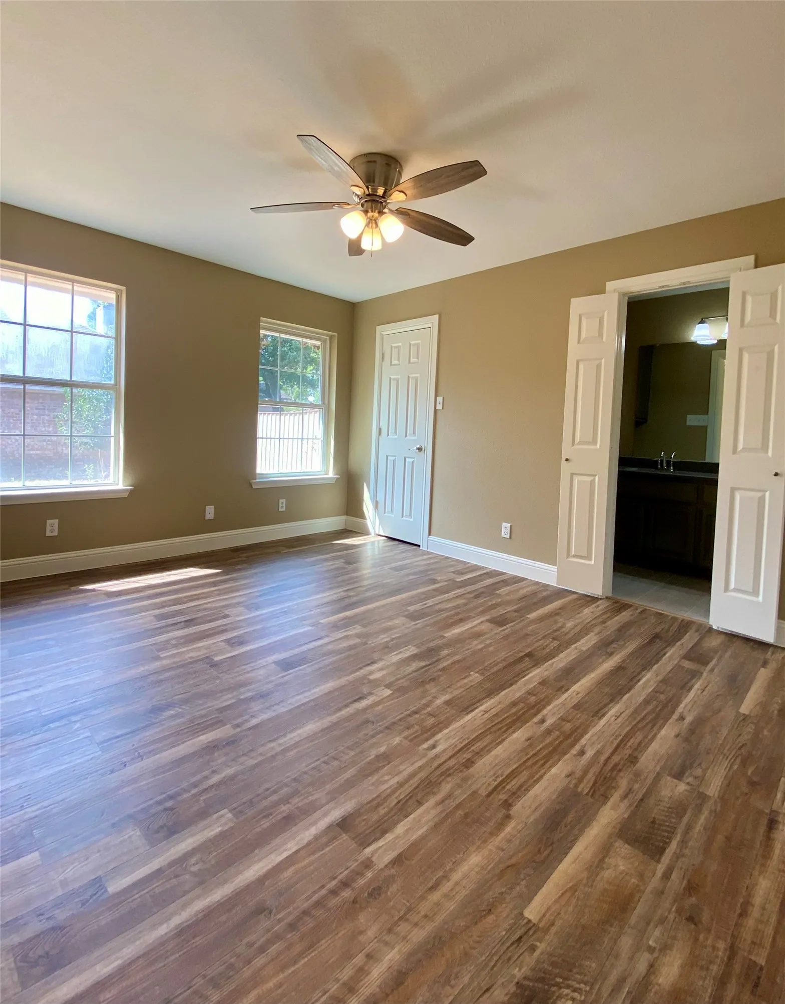 Wood-finish flooring, ceiling fan with integrated lighting, multiple windows, and a bathroom entry with bifold doors