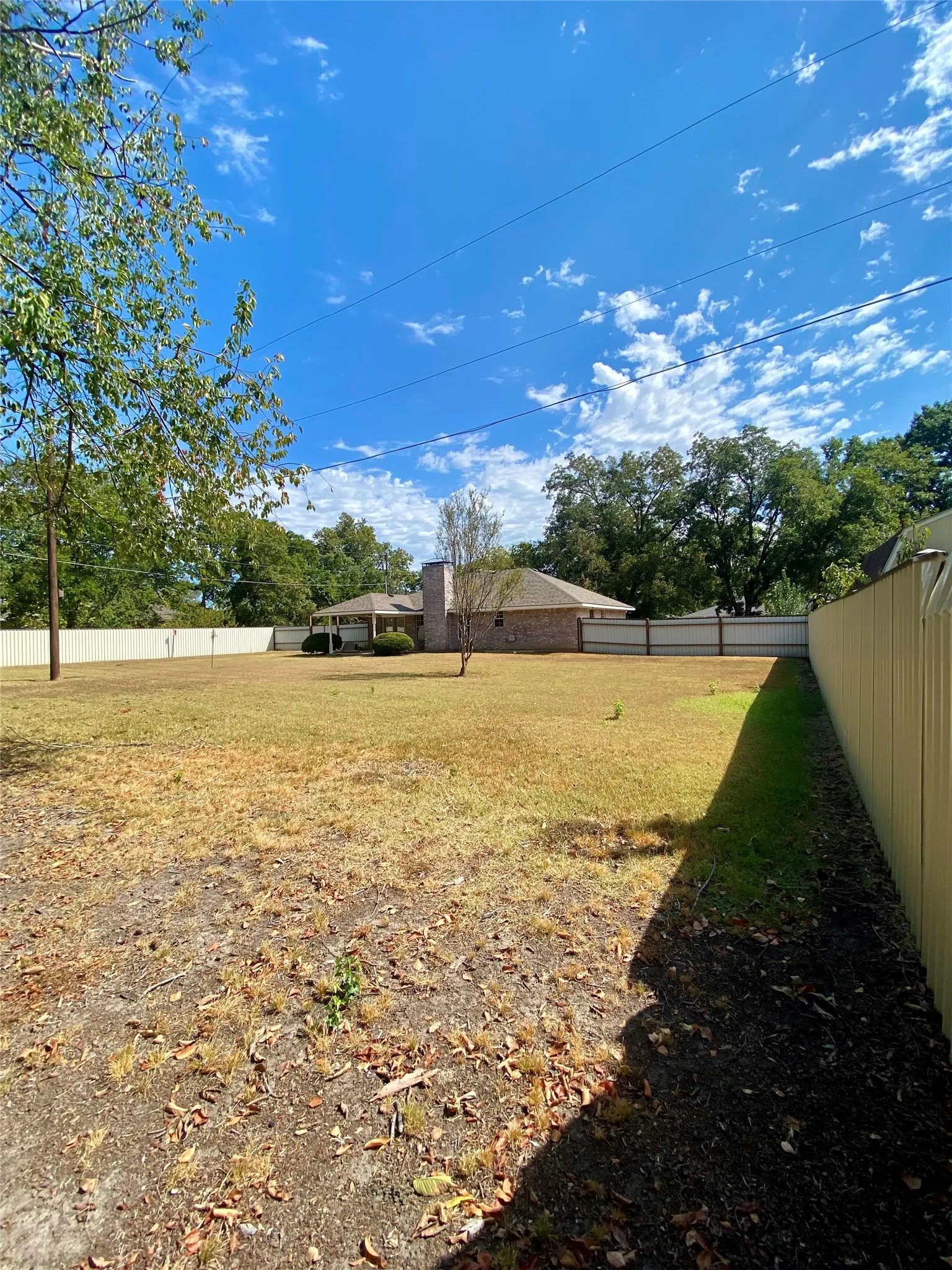 SW corner of Expansive backyard featuring a privacy fence, mature trees, and a brick exterior dwelling with a prominent chimney