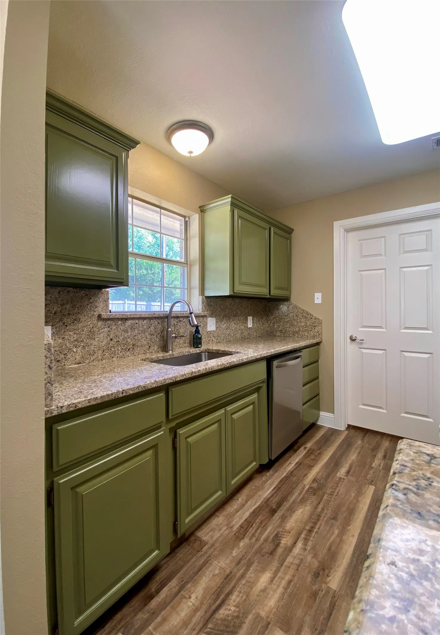 Green painted cabinetry with brushed nickel hardware, stone-look countertops, stainless steel sink with a gooseneck faucet, stainless steel dishwasher, and wood-finish flooring