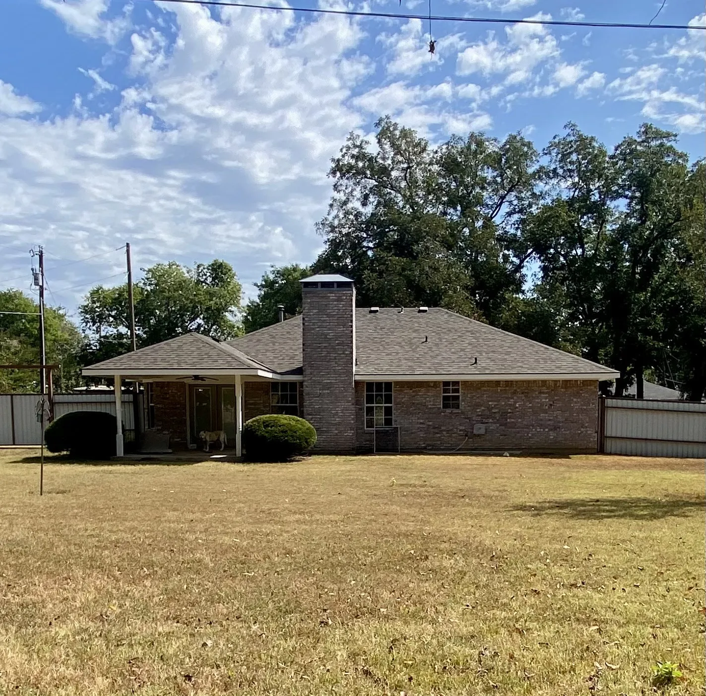 West elevation brick-clad residence featuring a covered patio, prominent brick chimney, and a fenced perimeter