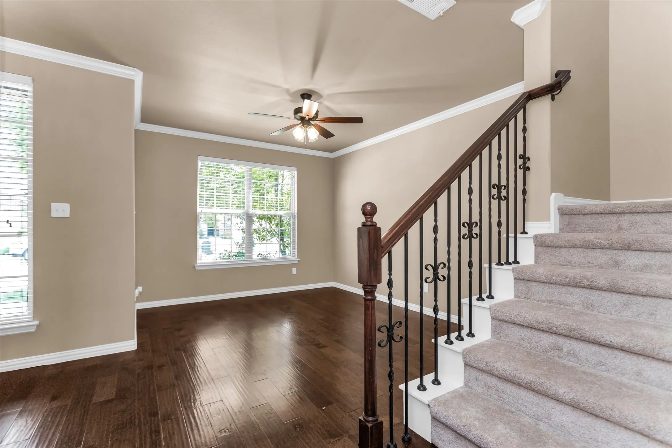 Hardwood flooring, crown molding, ceiling fan, and staircase with wrought iron balusters