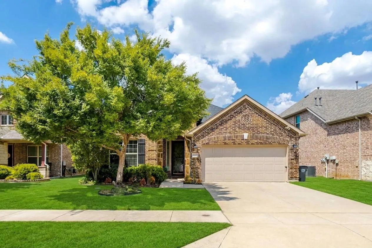 Brick exterior with stone accents, attached two-car garage, concrete driveway, and front lawn with mature landscaping