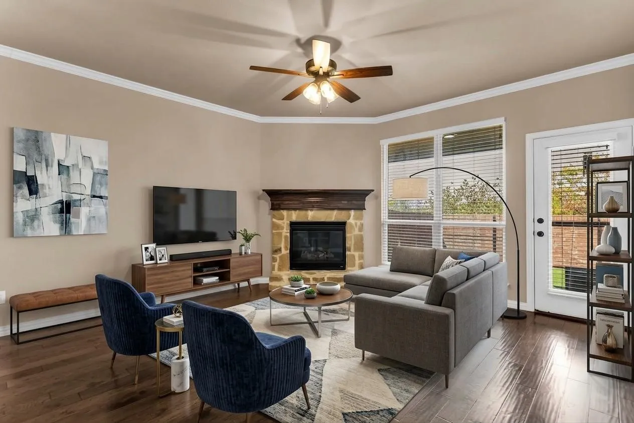Hardwood-style flooring, stone-faced fireplace with wood mantel, ceiling fan with integrated lighting, multiple windows, and a glass-paneled exterior door