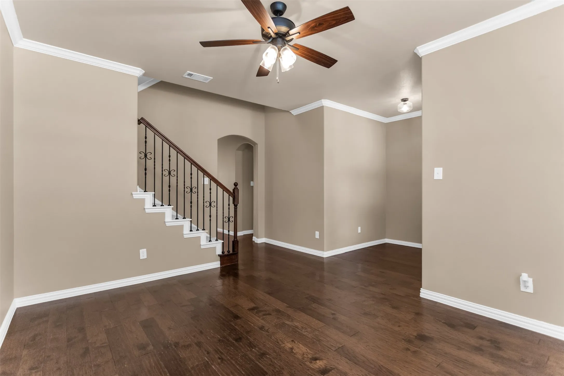 Hardwood-finish flooring, staircase with wrought iron balusters, crown molding, arched doorway, and a ceiling fan with integrated lighting