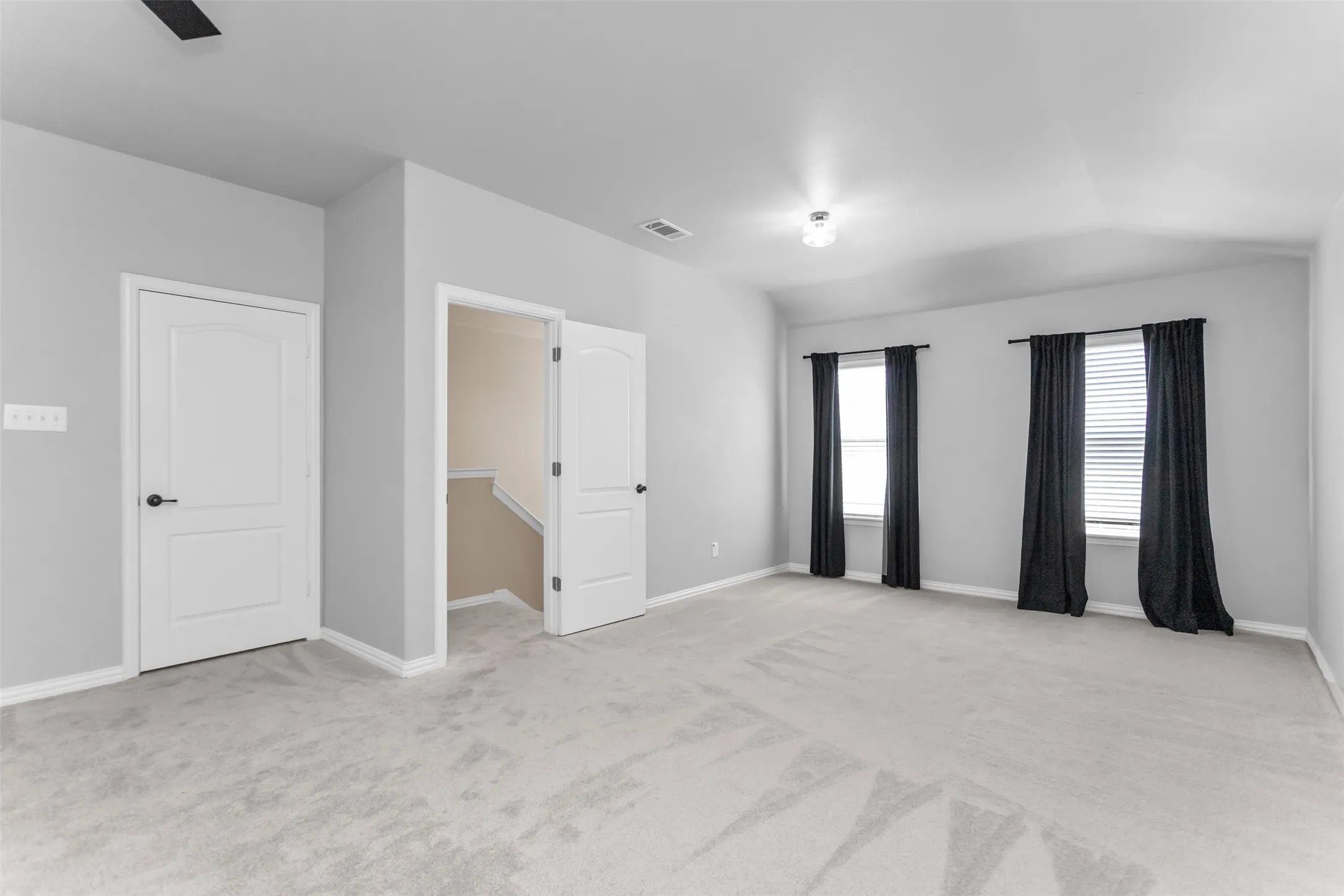 Spacious room featuring light gray carpeting, neutral wall color, multiple windows with blinds, a ceiling-mounted light fixture, and white interior doors