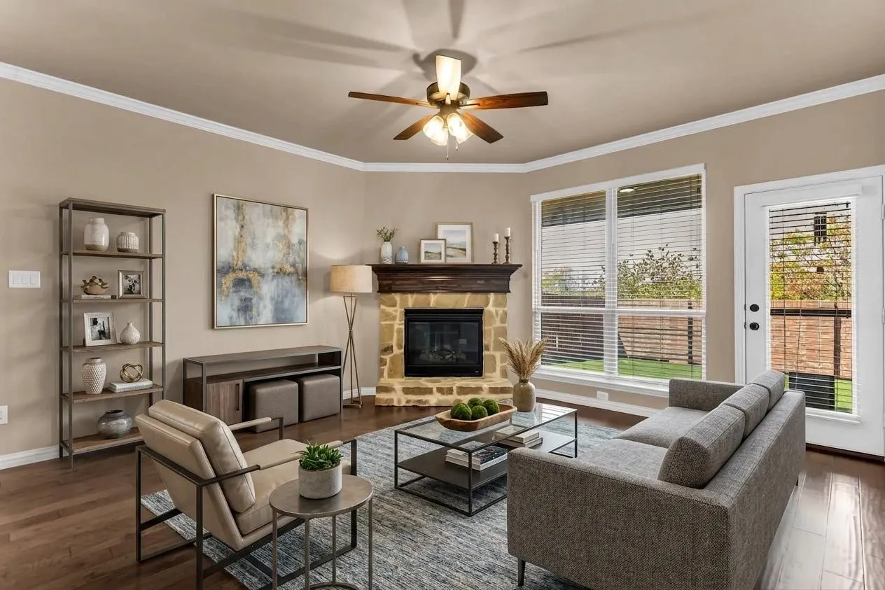 Hardwood flooring, stone-clad fireplace with mantel, crown molding, ceiling fan, and large windows with blinds