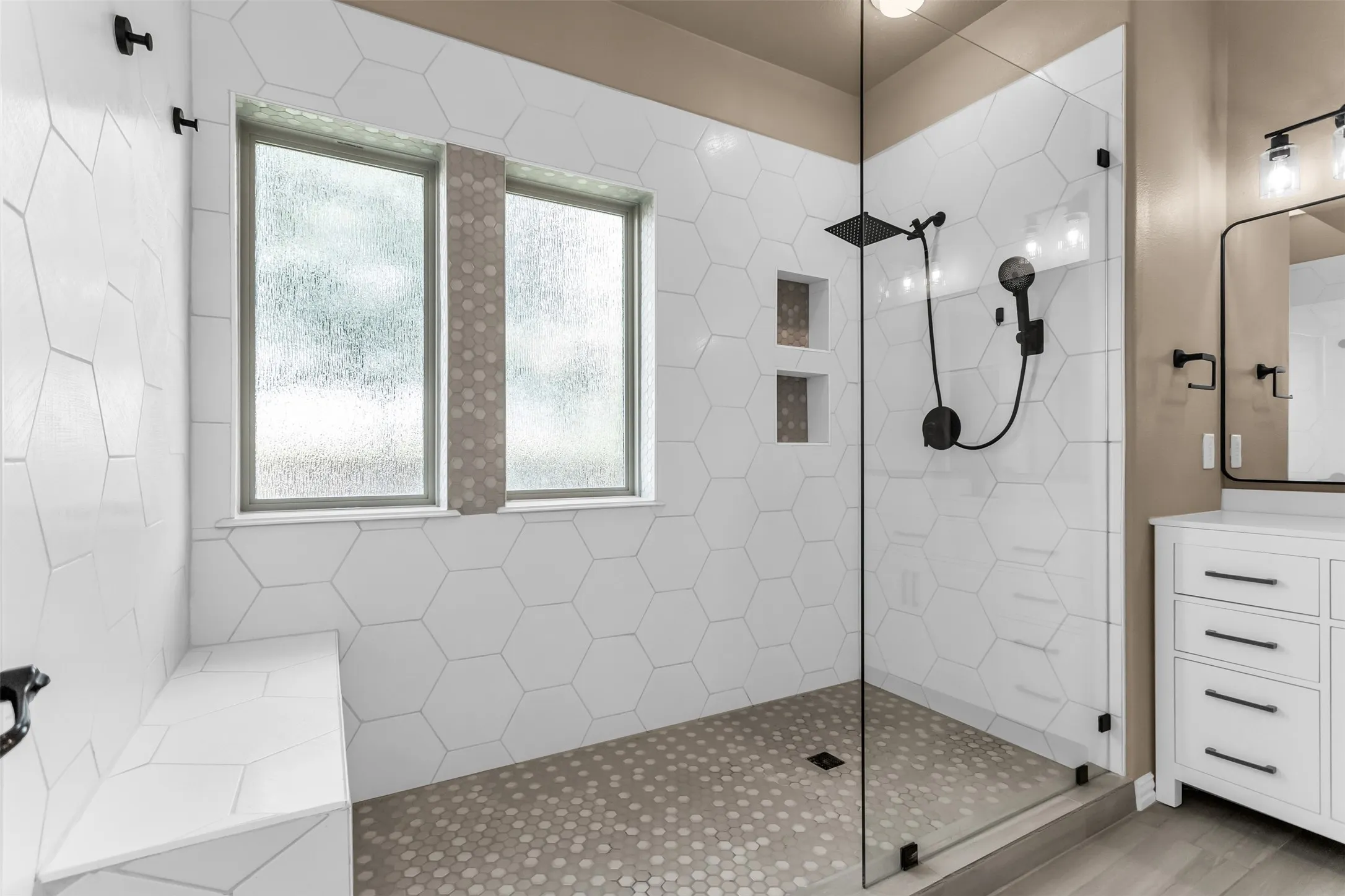 Glass-enclosed shower with a rainfall showerhead, integrated tiled bench, and dual recessed niches