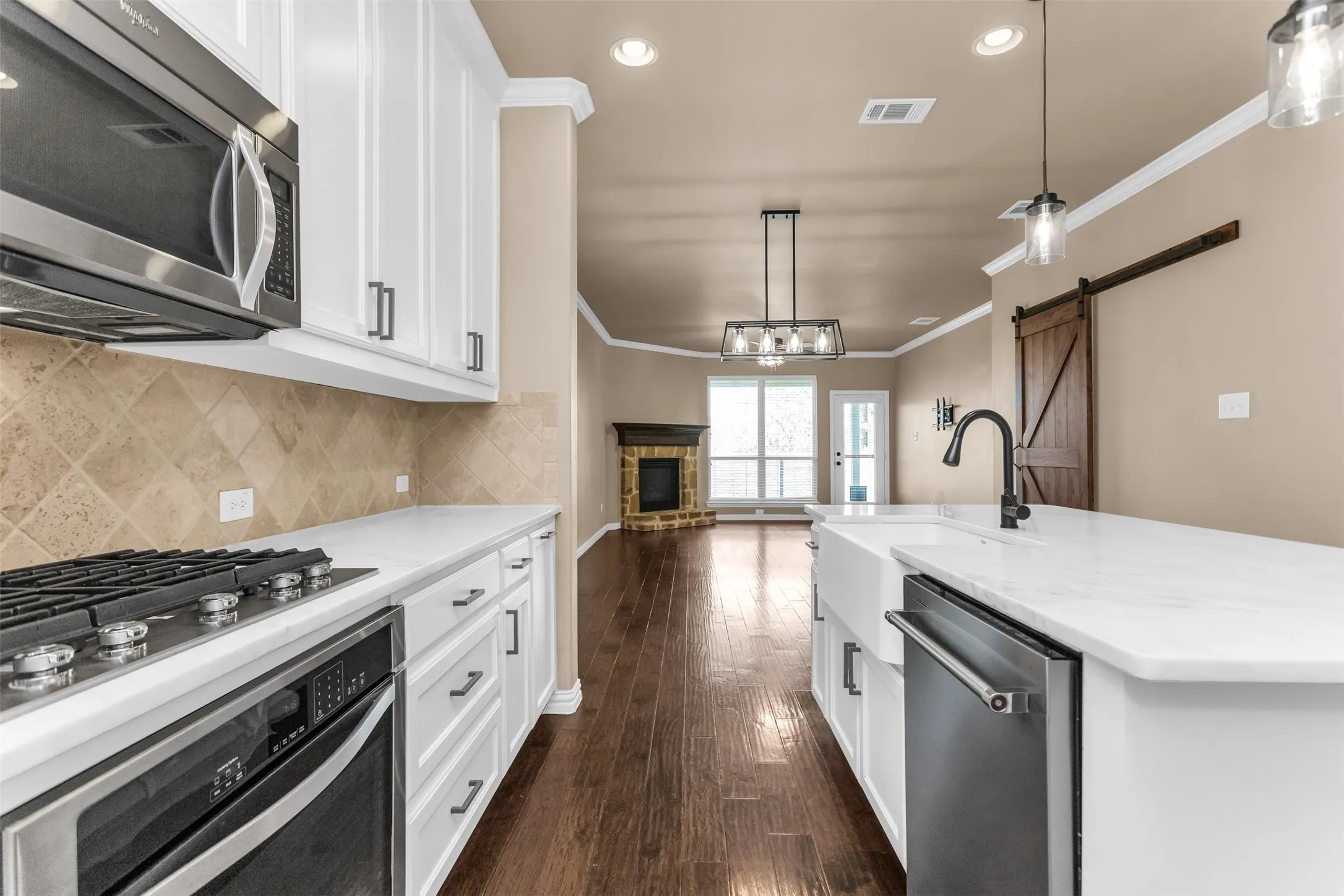 White shaker cabinetry with black hardware, stainless steel appliances, white countertops, farmhouse sink with gooseneck faucet, and wood-finish flooring