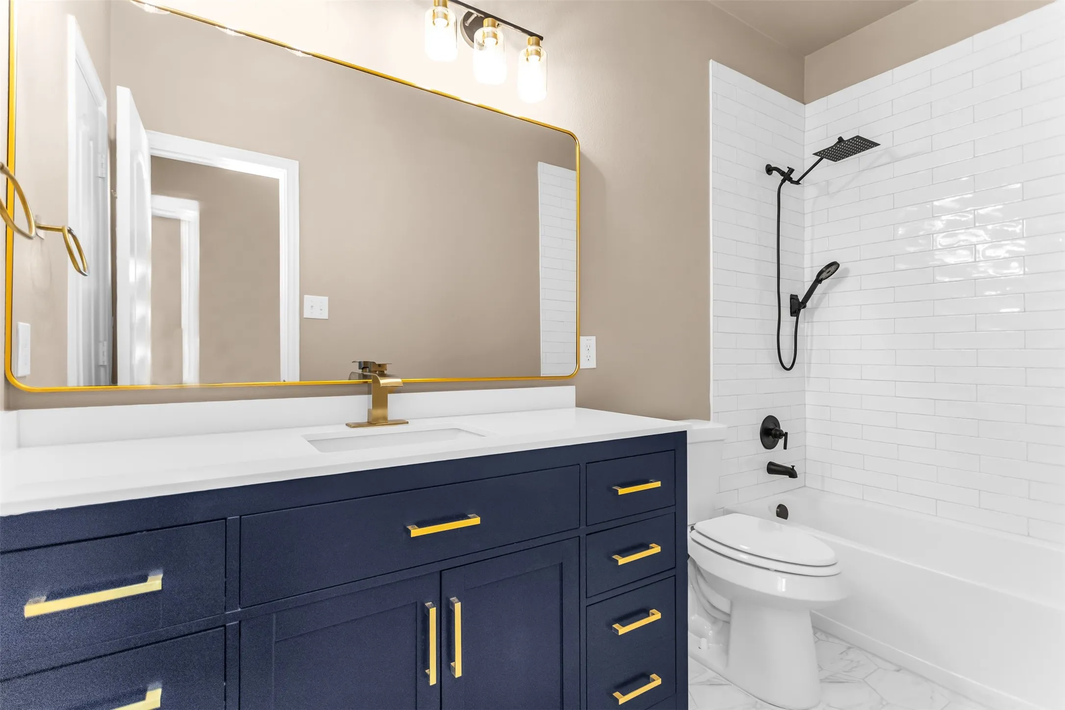 Navy vanity with gold hardware, white countertop, gold-framed mirror, and white subway tile shower surround with black fixtures