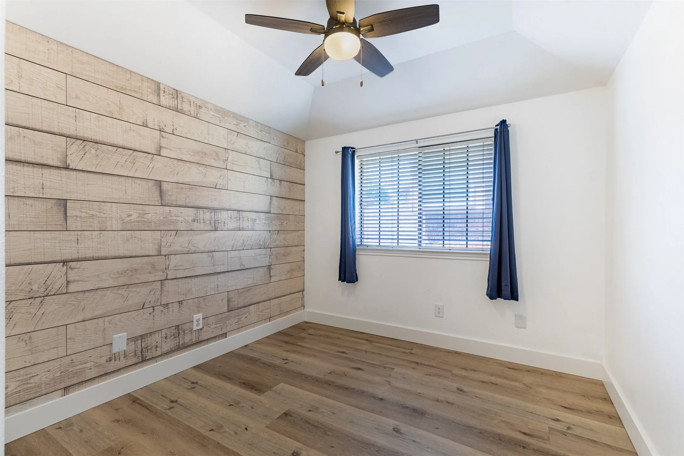 Upstairs secondary bedroom with wood accent wall and ceiling fan.