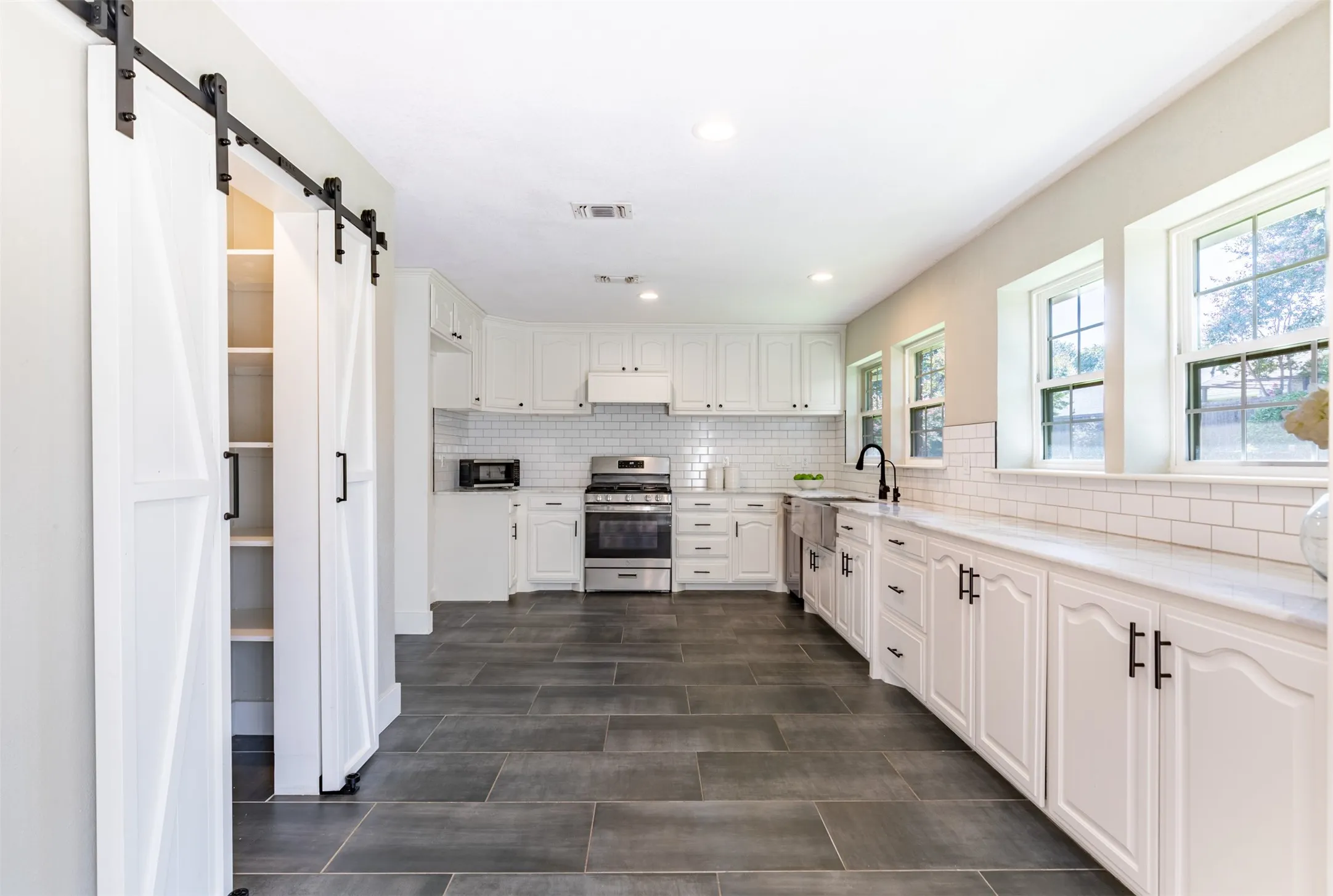 Kitchen features pristine white cabinetry and sliding barn doors to pantry.