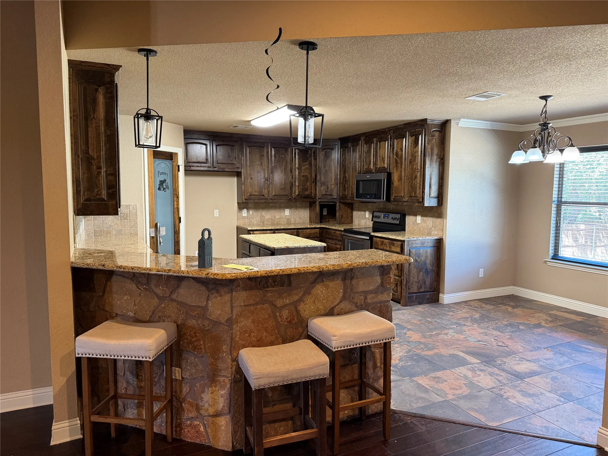 Kitchen featuring wood cabinetry, stone veneer breakfast bar, granite countertops, and tile flooring