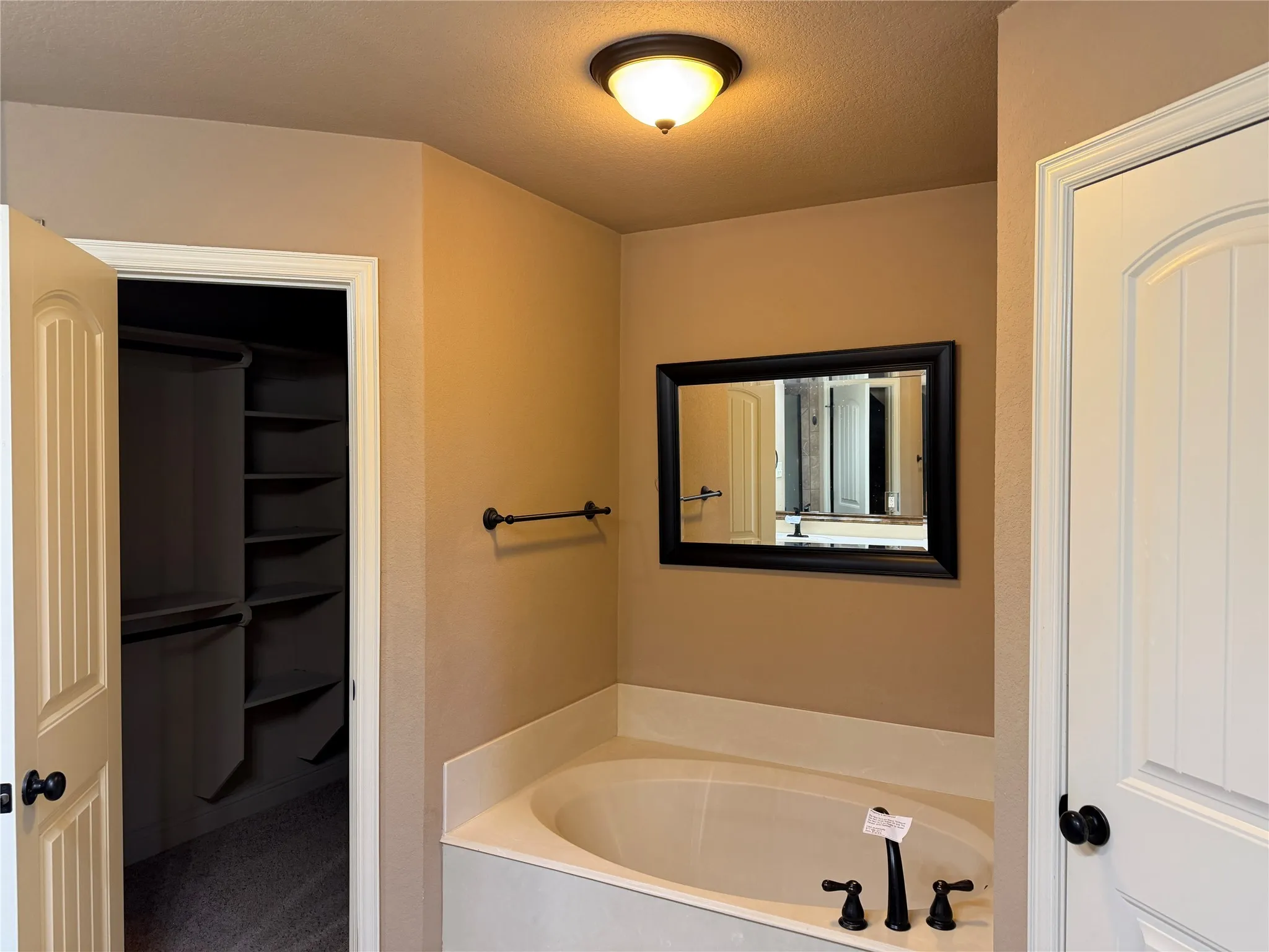 Built-in tub with matte black fixtures, framed wall mirror, and dedicated closet with shelving