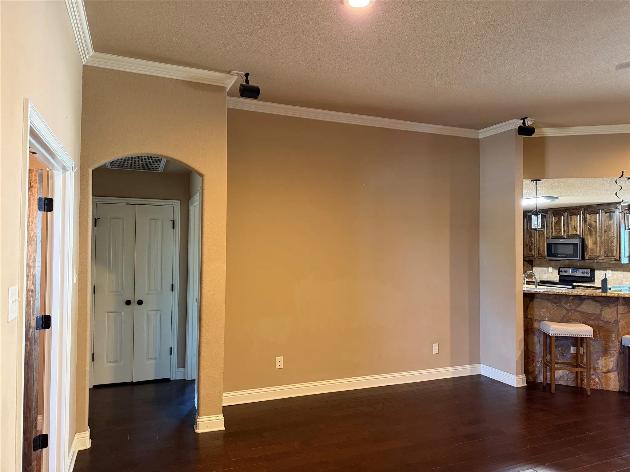 Wood-finish flooring with white baseboards, crown molding, arched doorway, and recessed lighting