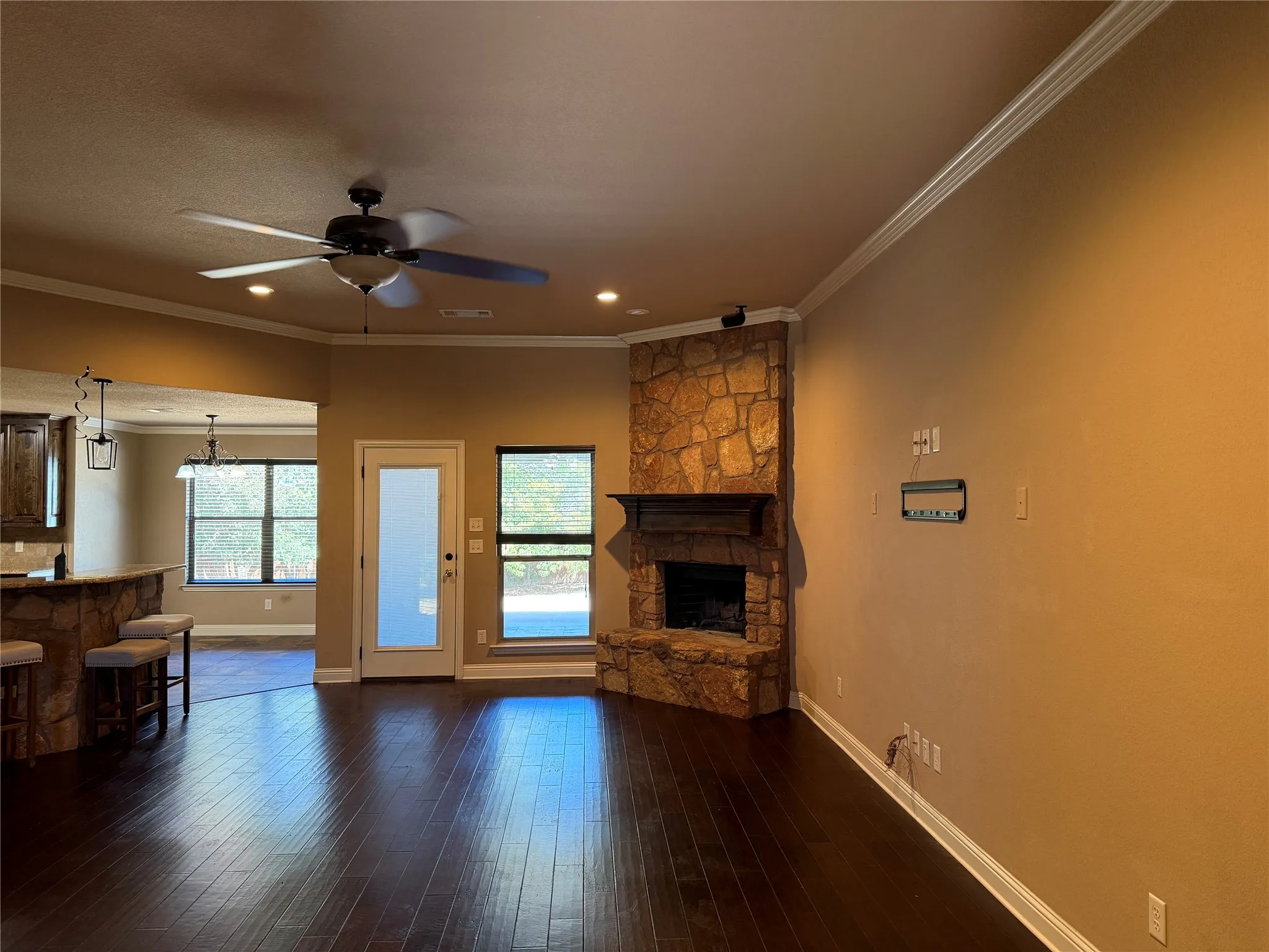 Dark wood-finish flooring, stone fireplace with wood mantel, built-in ceiling lighting, and crown molding