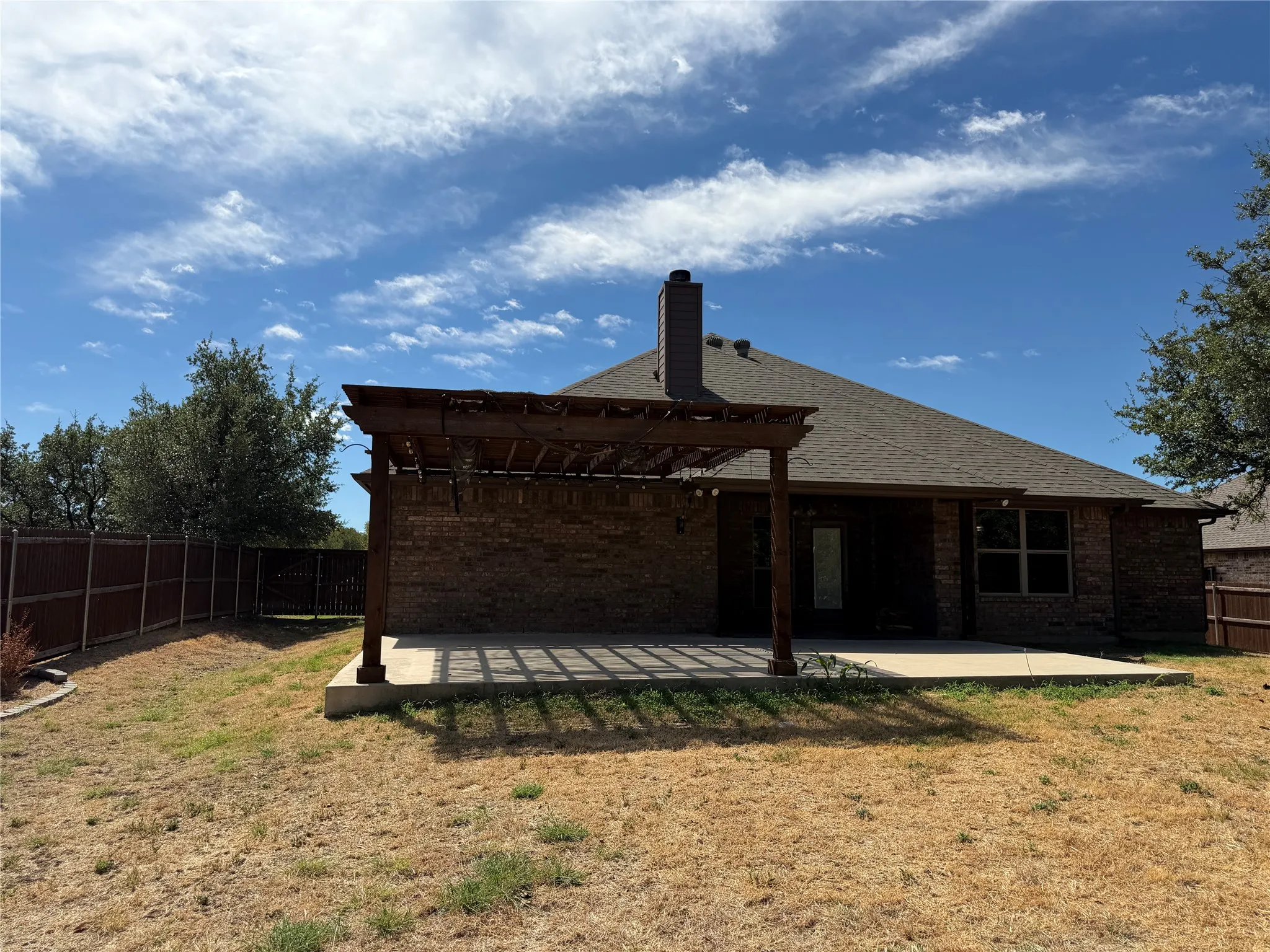 Expansive concrete patio with a wooden pergola, brick exterior, and a shingled roof