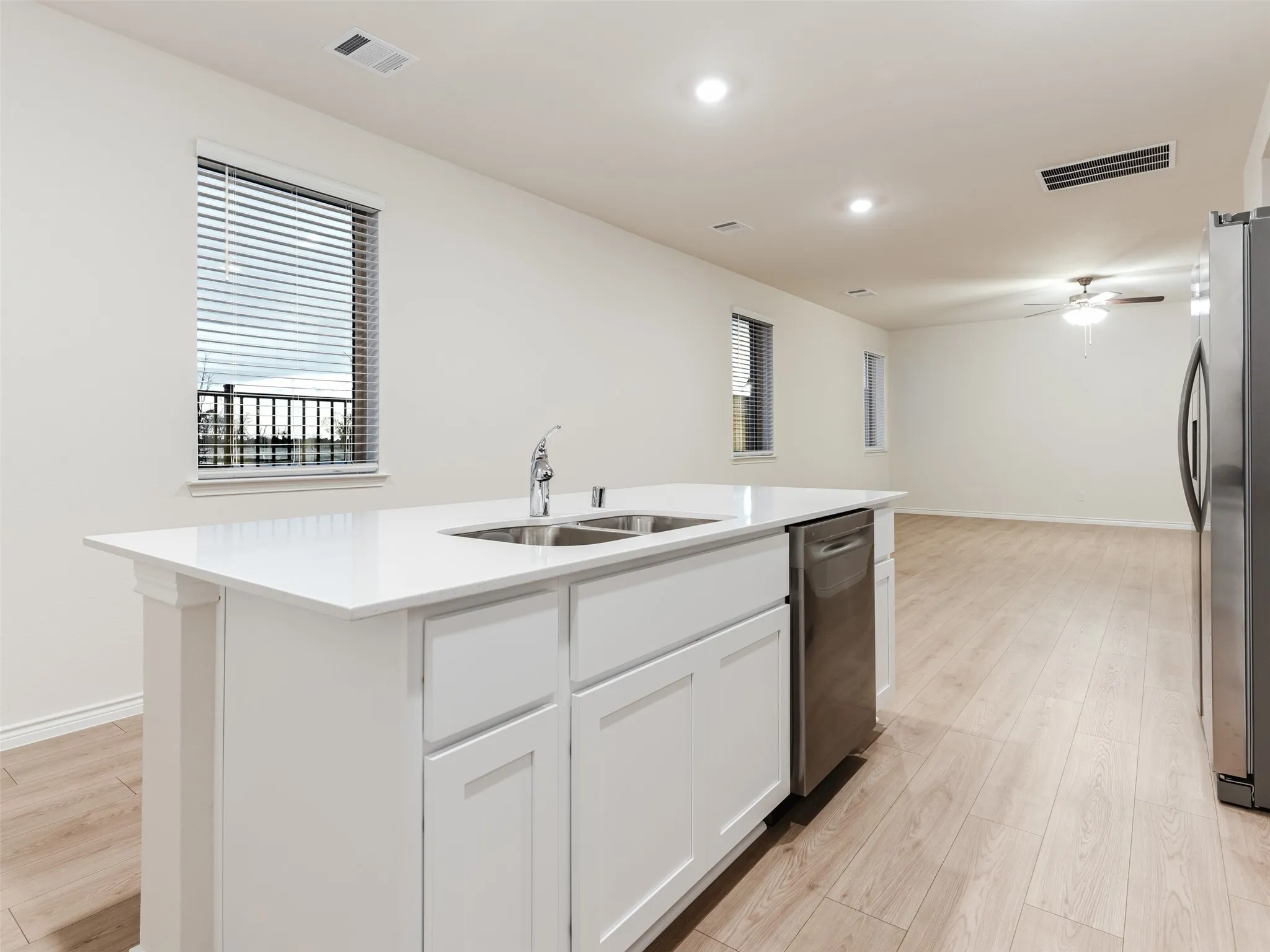 Kitchen island with a white countertop and integrated dual-basin sink, stainless steel dishwasher, and wood-finish flooring
