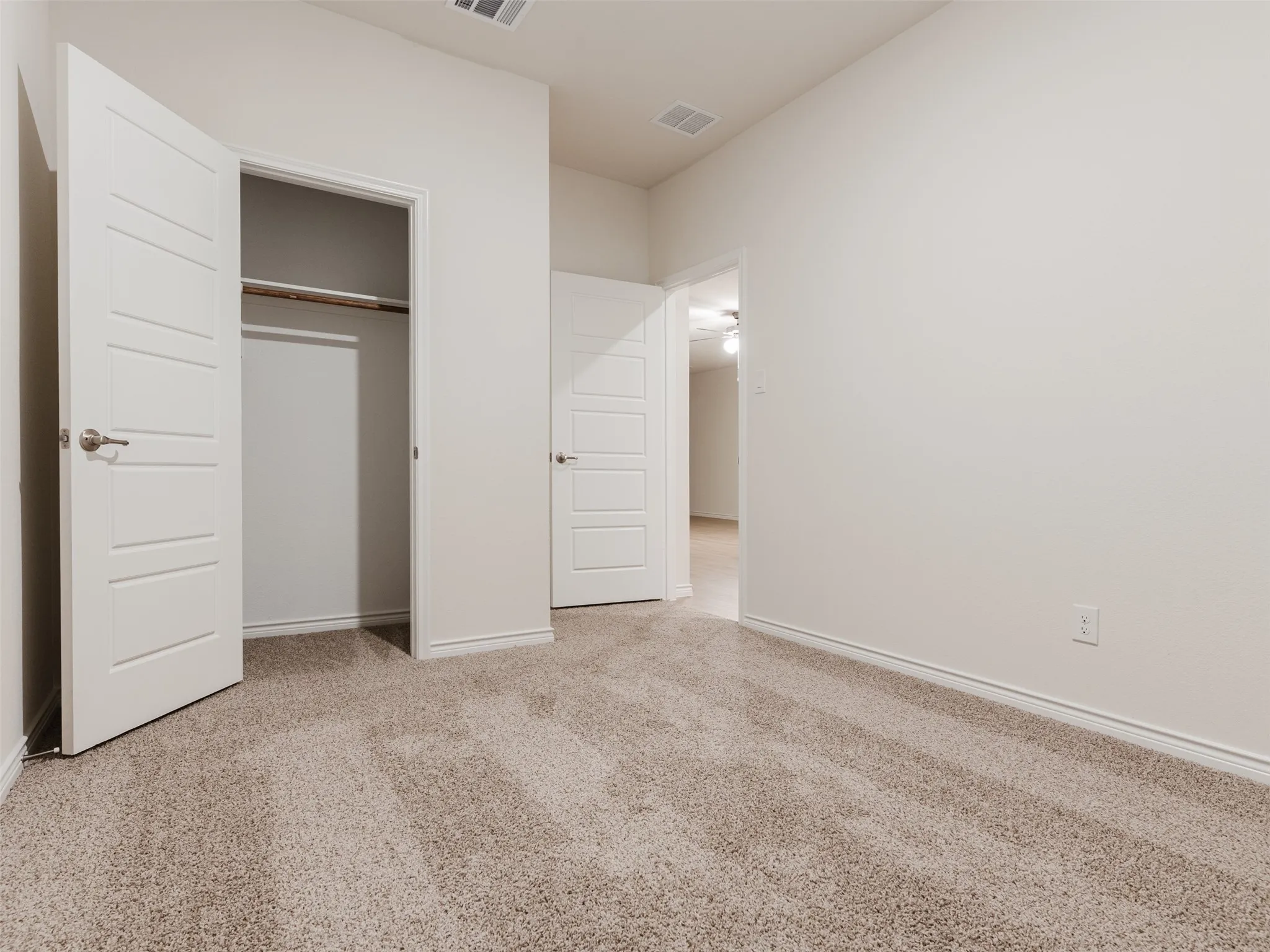 Neutral tone wall paint, light neutral carpet, white paneled interior doors, and a built-in closet with hanging rod