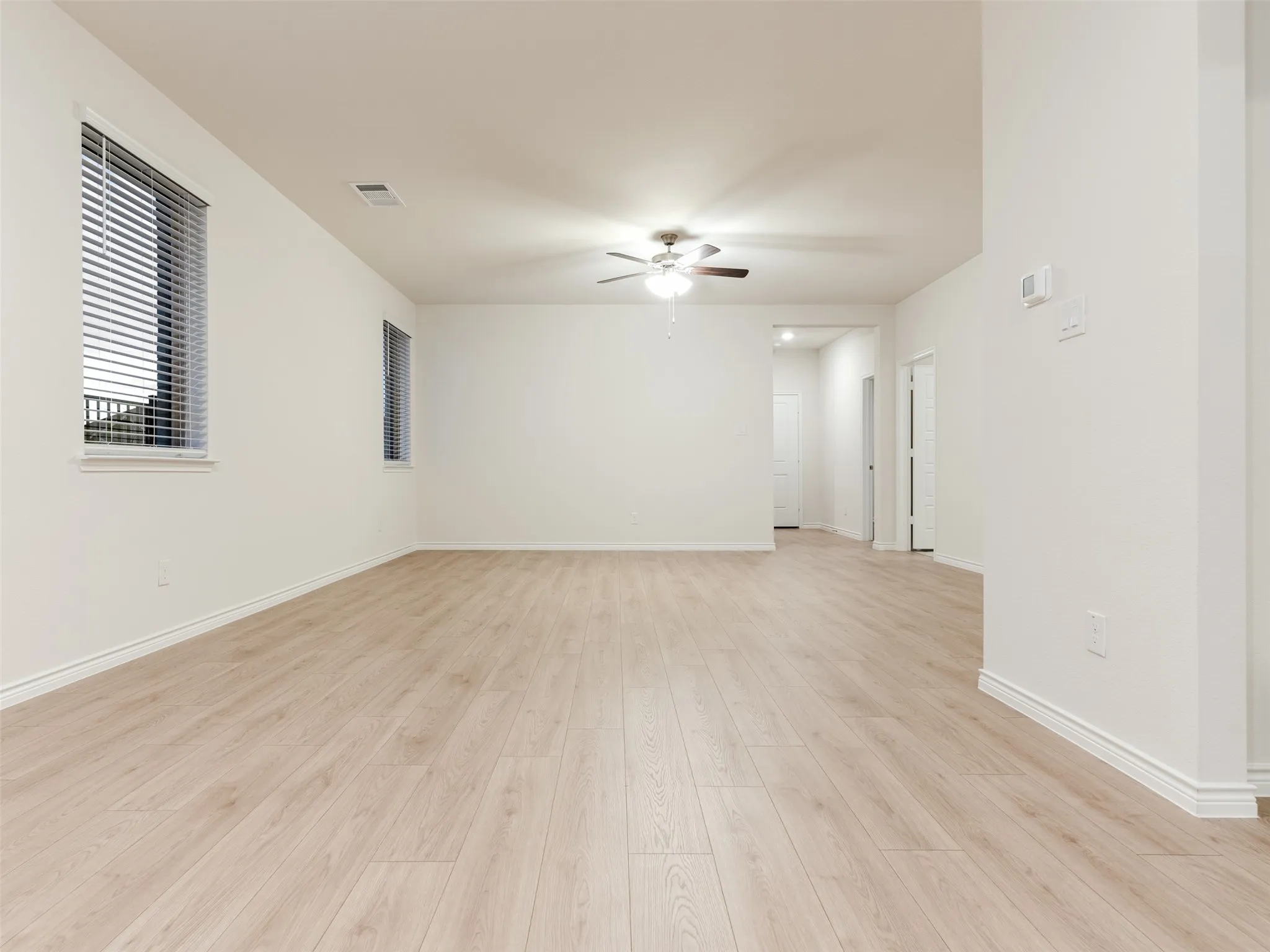 Wood-finish flooring throughout, multiple windows with blinds, recessed lighting, and a ceiling fan with integrated lighting