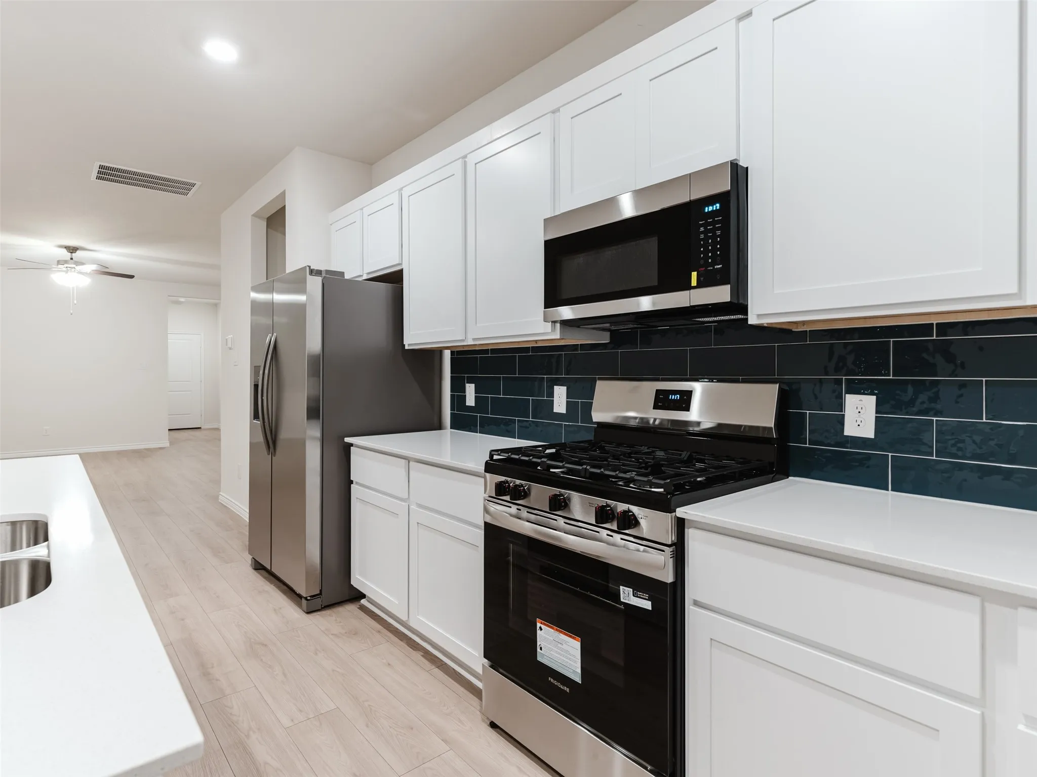 Kitchen featuring white shaker-style cabinetry, stainless steel appliances, a dark subway tile backsplash, and light-toned wood-finish flooring