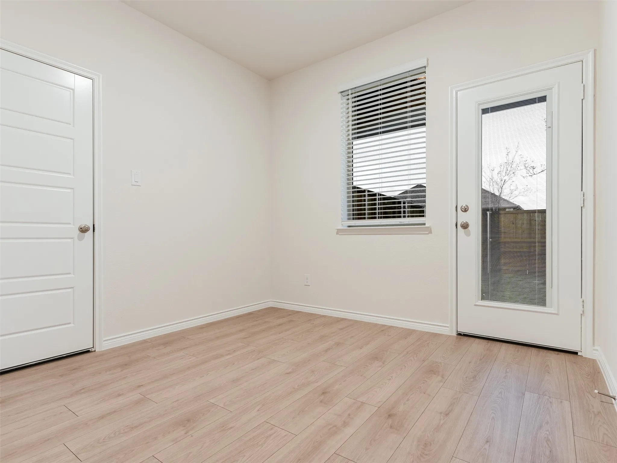 Light wood-finish flooring, white walls, a multi-panel interior door, a window with blinds, and an exterior door with glass paneling