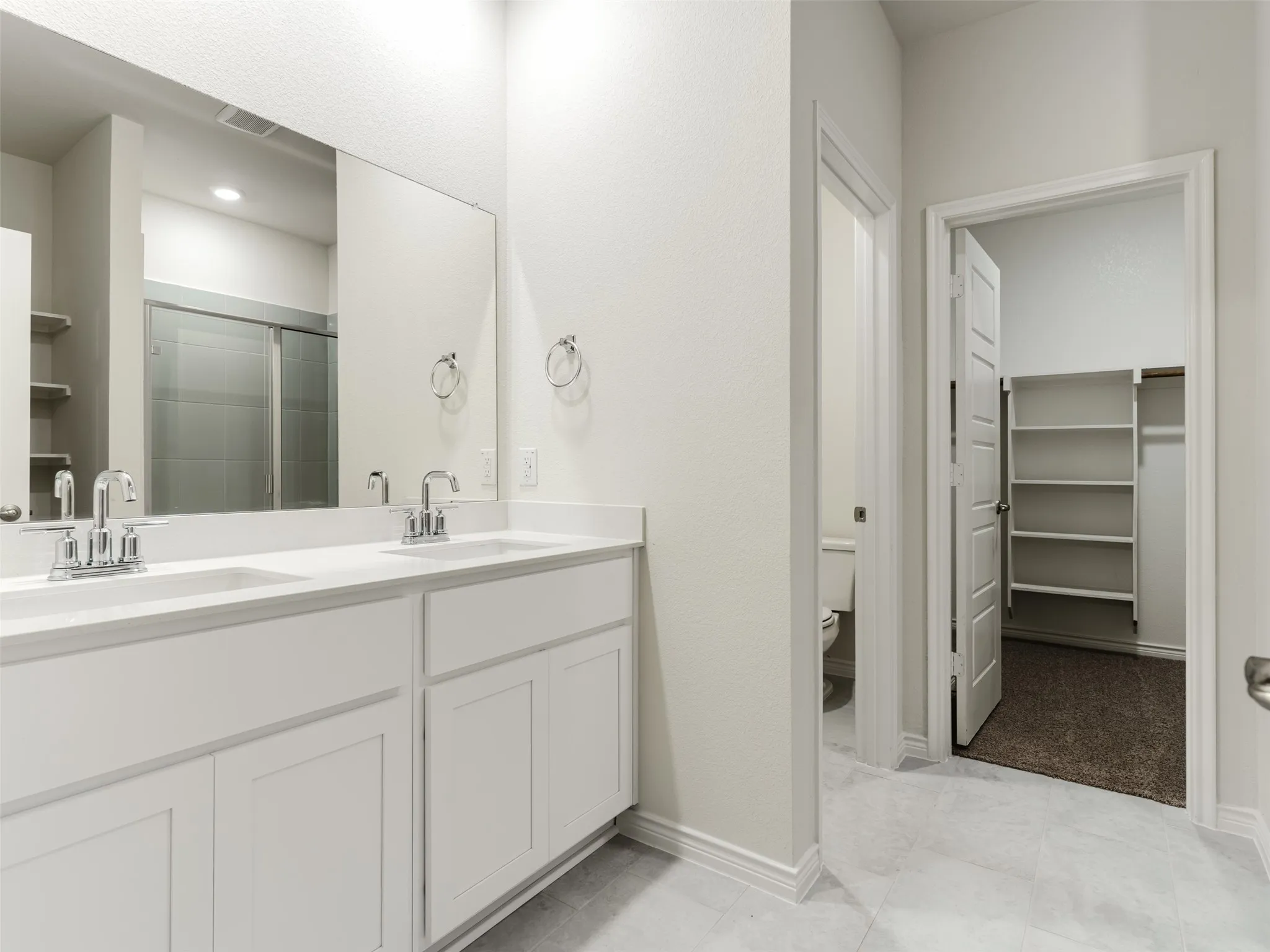 Dual sink vanity with white cabinetry, polished chrome fixtures, and a large wall-mounted mirror