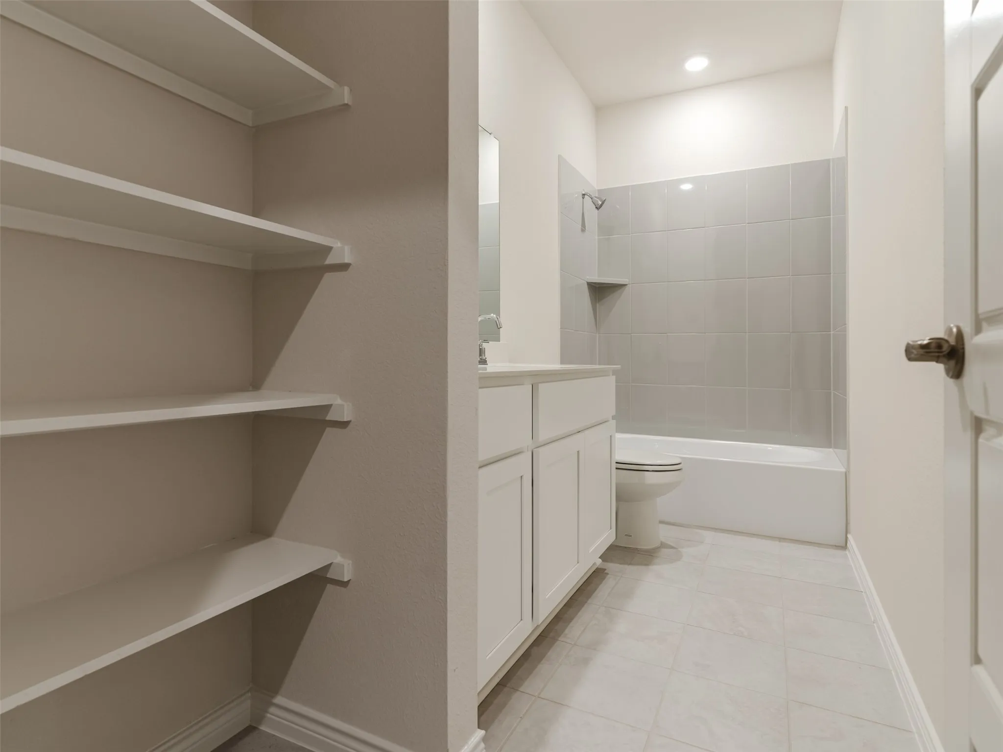 Built-in shelving, white single vanity with cabinet storage, tile flooring, and a shower-tub combination with tiled surround