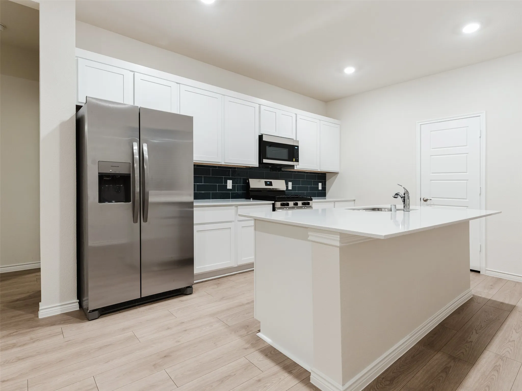 Modern kitchen featuring a central island with an undermount sink, white cabinetry, dark subway tile backsplash, stainless steel appliances, and wood-finish flooring