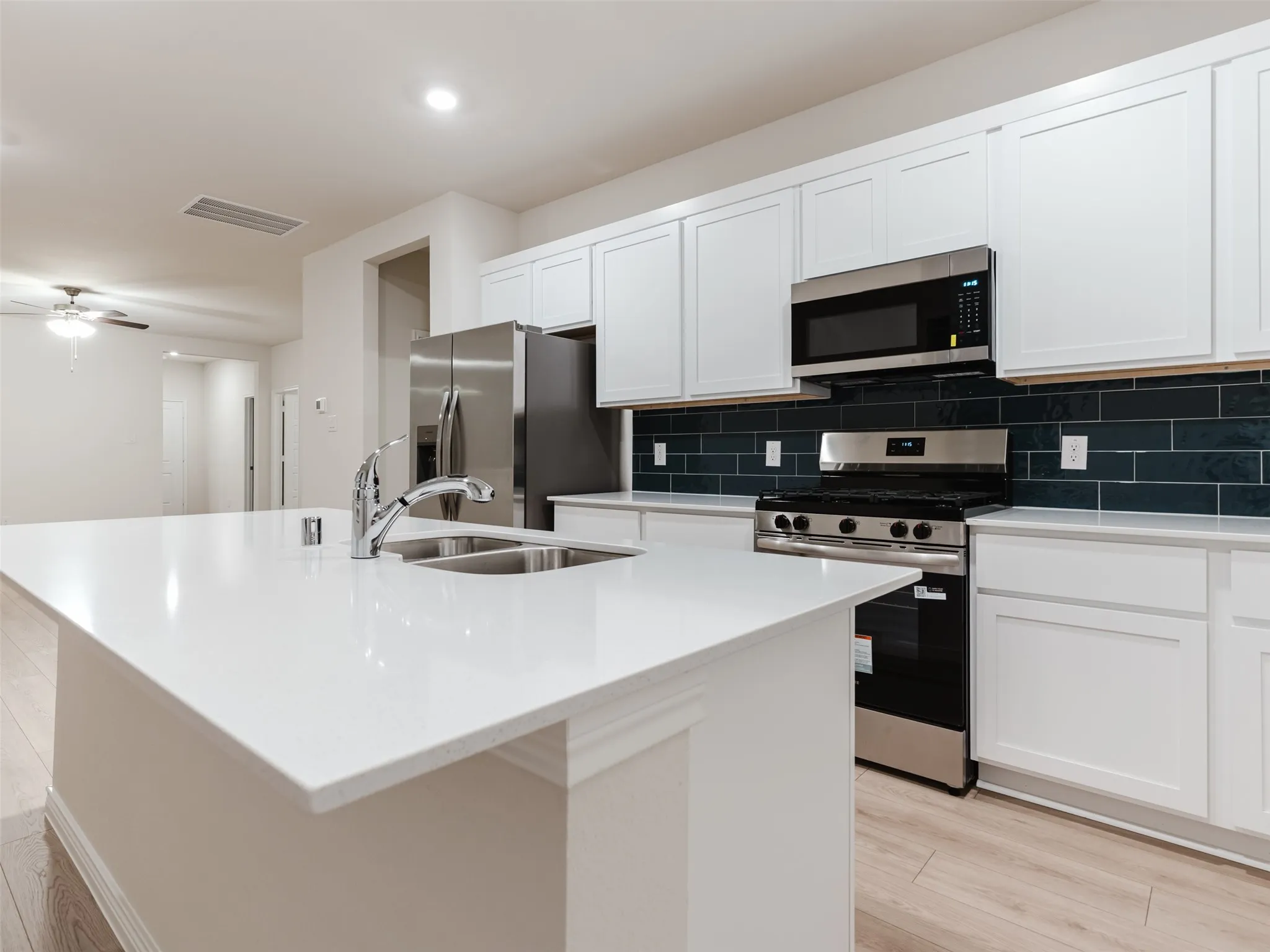 Kitchen featuring a white countertop island with a double basin sink, stainless steel appliances, dark subway tile backsplash, and white cabinetry