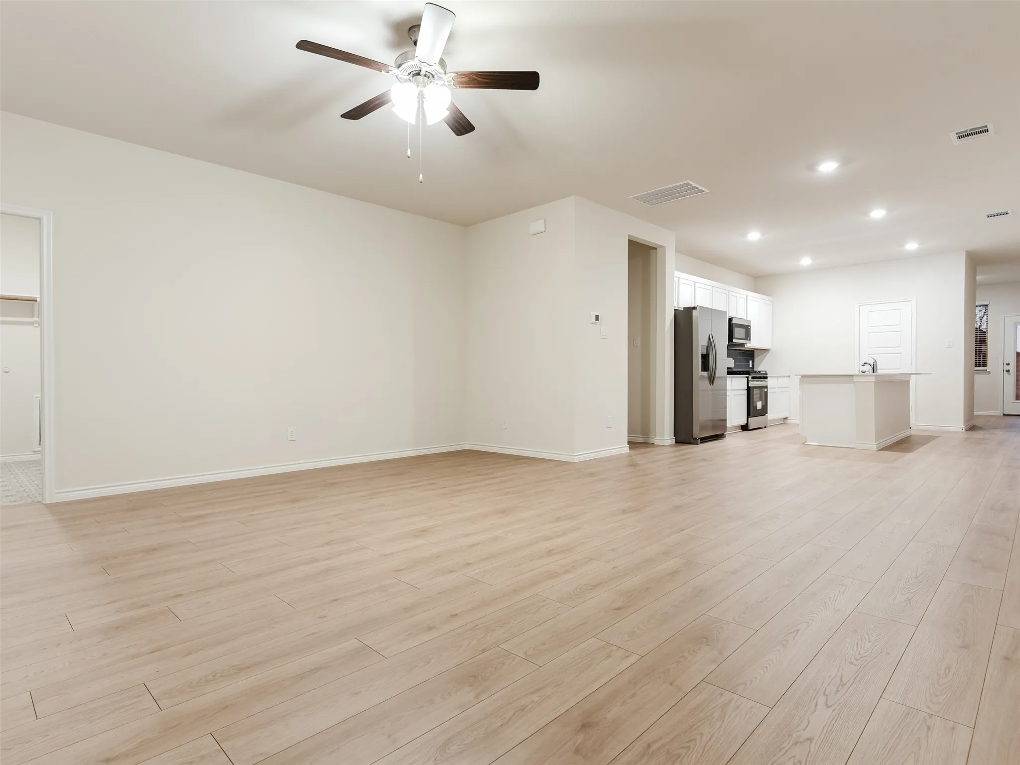 Spacious interior featuring wood-finish flooring, ceiling fan, recessed lighting, and a kitchen with stainless steel appliances and an island