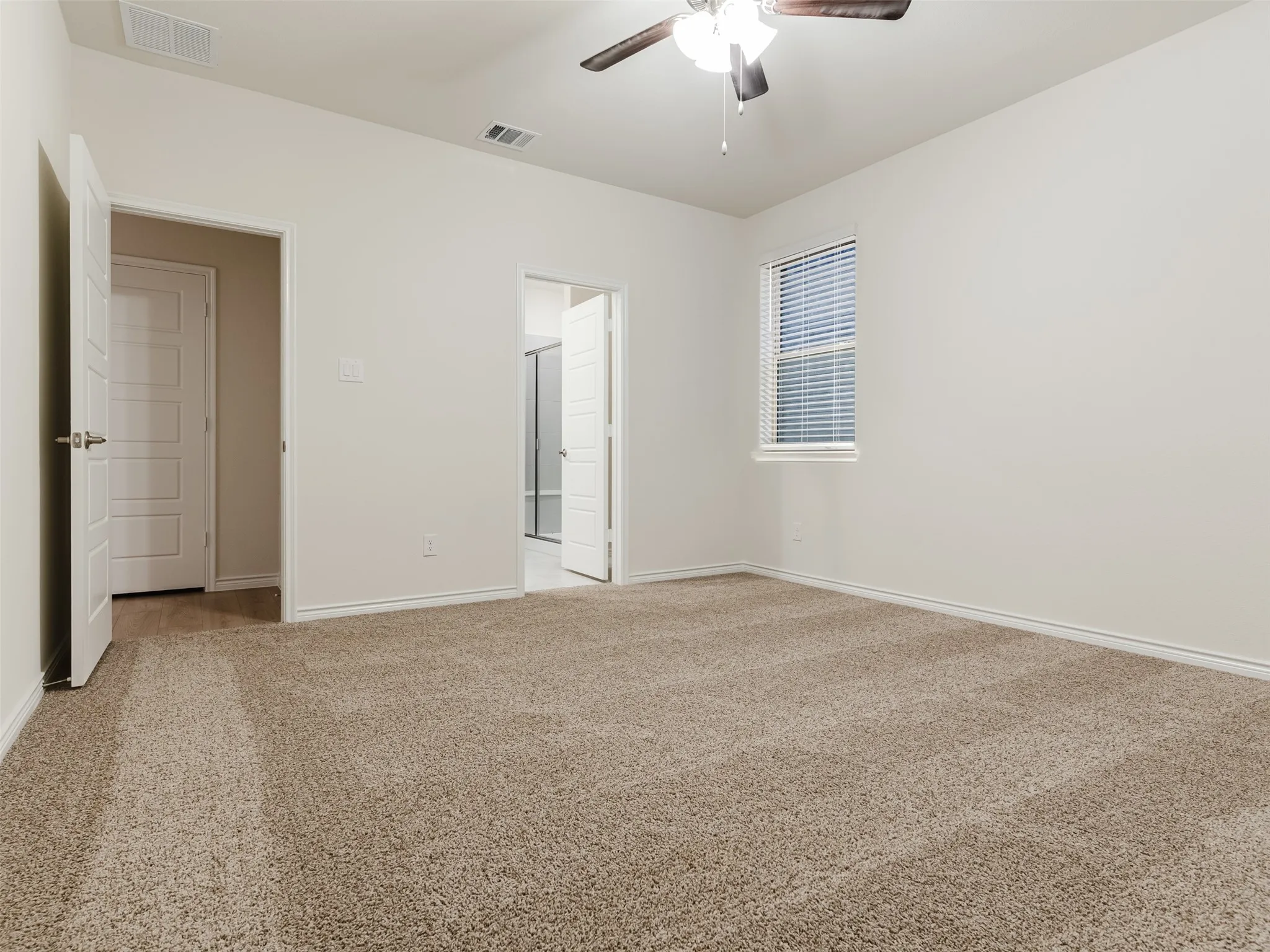 Spacious room featuring neutral carpeting, a ceiling fan with integrated lighting, and a window with blinds