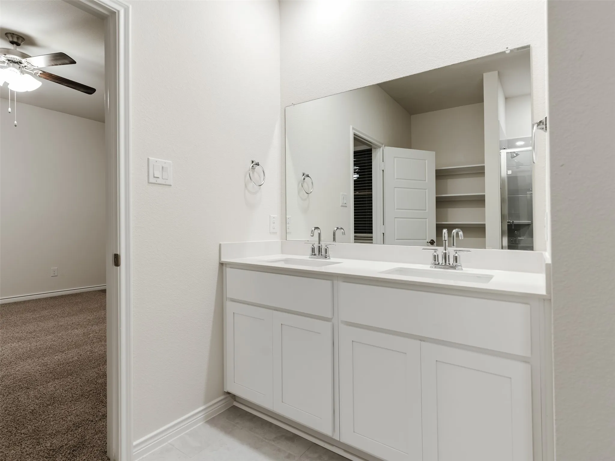 Dual sink vanity with white cabinetry and chrome fixtures, large wall-mounted mirror, and tile flooring