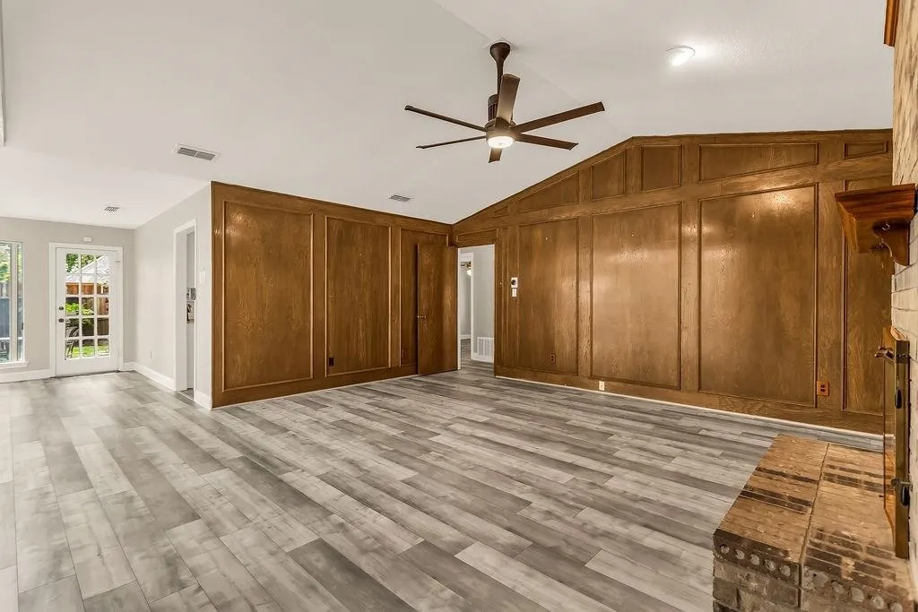 Vaulted ceiling with a ceiling fan, wood-finish paneling, brick fireplace, and wood-finish flooring