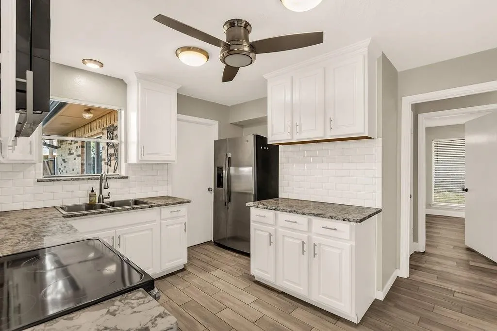 White cabinetry with dark hardware, subway tile backsplash, stone-finish countertops, wood-look flooring, and stainless steel appliances