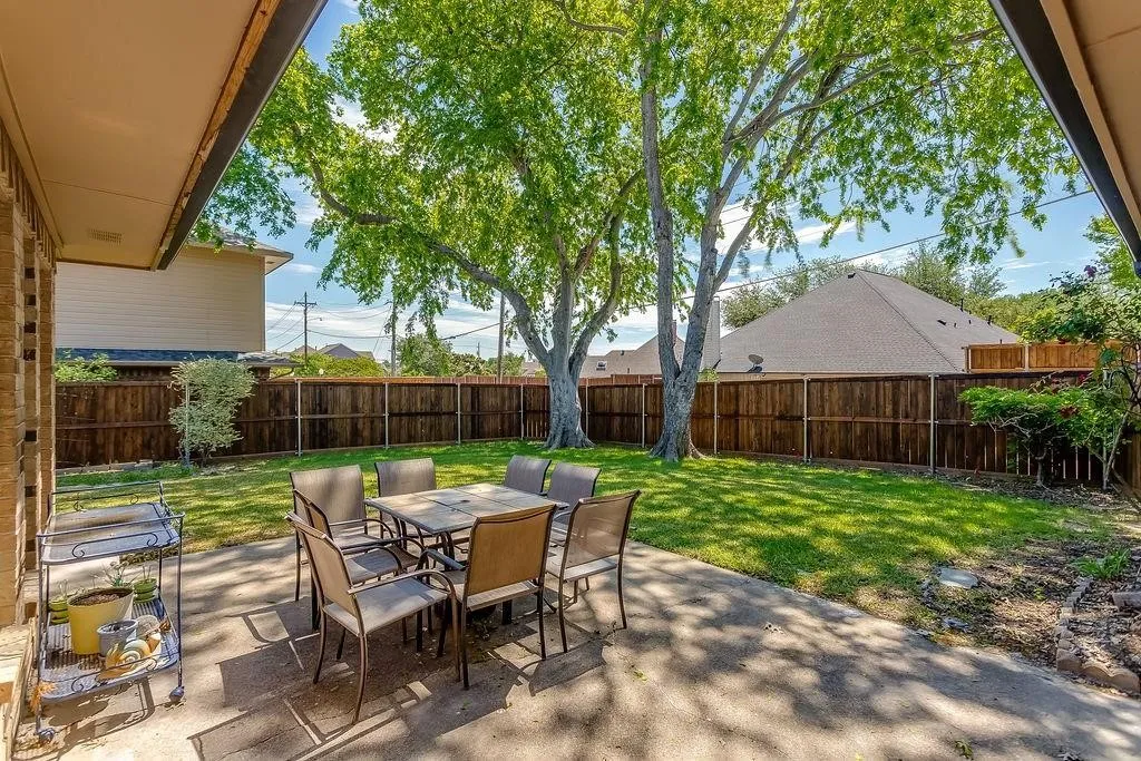 Expansive backyard oasis featuring a mature shade tree, manicured lawn, and wooden privacy fencing