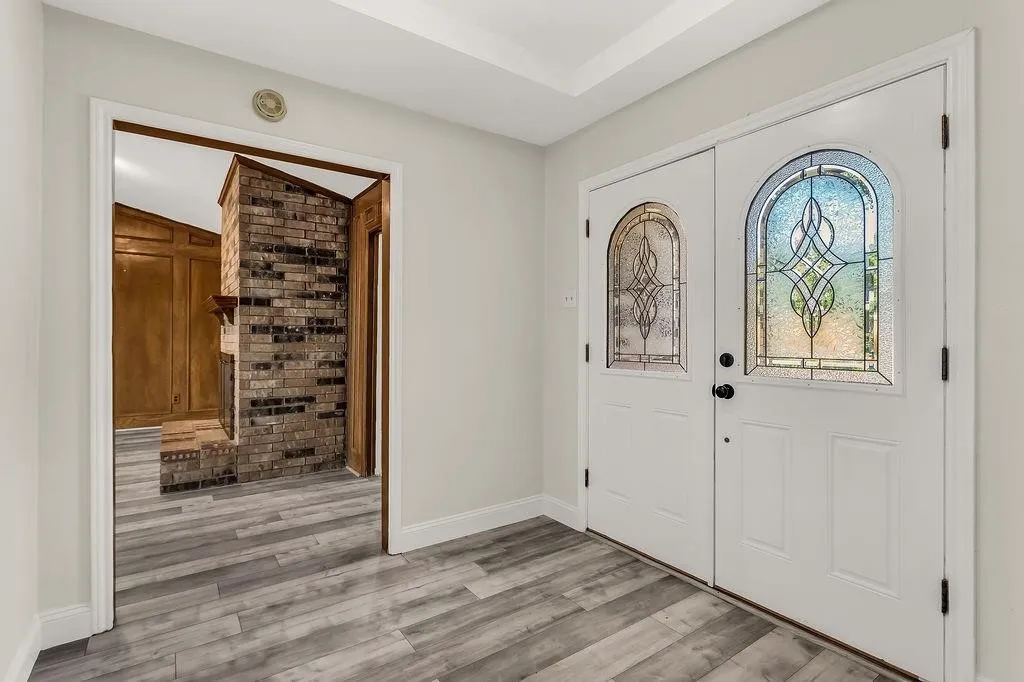 Double entry doors with decorative glass panels, wood-finish flooring, and crown molding
