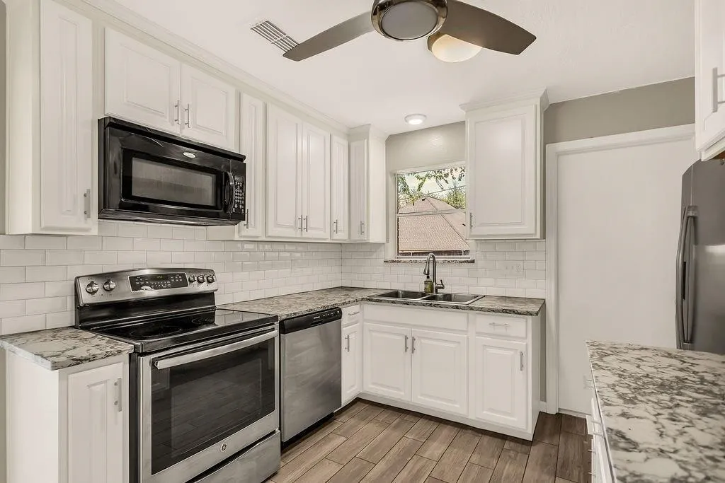 White cabinetry with brushed nickel hardware, subway tile backsplash, stainless steel appliances, wood-finish flooring, and a ceiling fan with integrated lighting