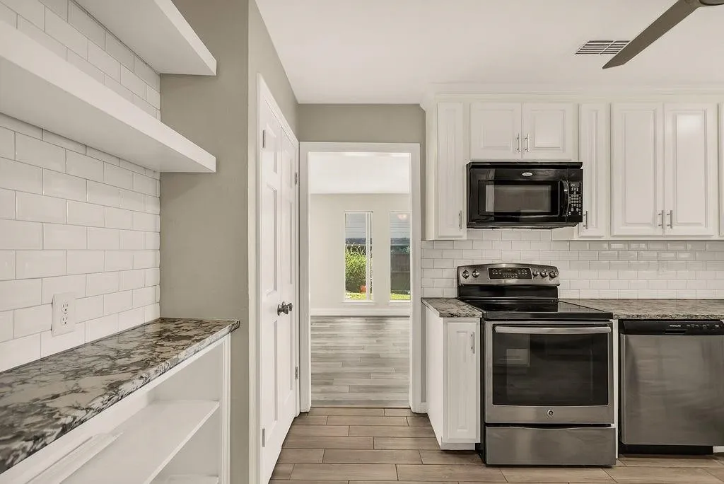 White shaker-style cabinetry, subway tile backsplash, stainless steel appliances, wood-finish flooring, and open shelving