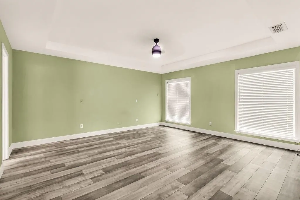 Tray ceiling accenting the room, wood-finish flooring, and multiple windows with blinds