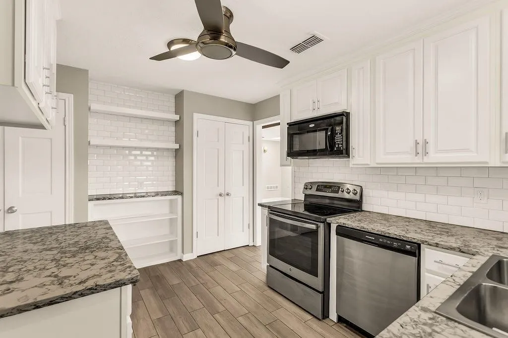 White cabinetry, wood-finish flooring, subway tile backsplash, stainless steel appliances, and built-in shelving