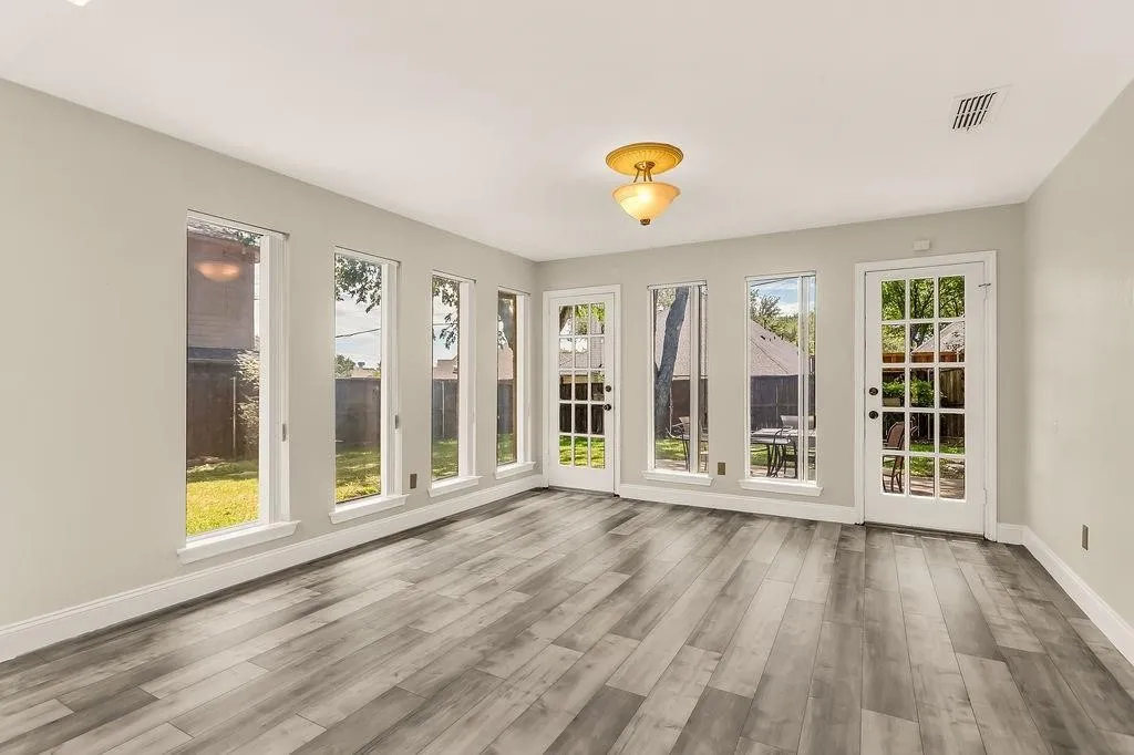 Wood-finish flooring, multiple tall windows, two French doors with grid-patterned glass, and a semi-flush mount ceiling light