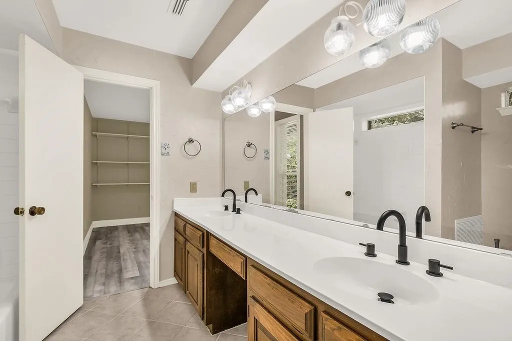 Dual undermount sinks with matte black fixtures, extensive vanity countertop, wood-finish cabinetry, and tiled flooring