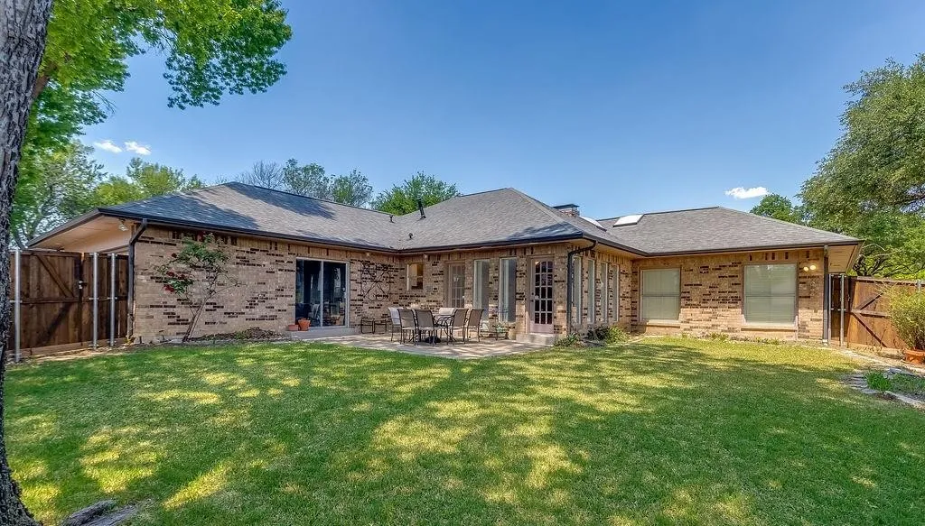 Expansive backyard featuring a manicured lawn, brick exterior, patio area, multiple windows, and a privacy fence