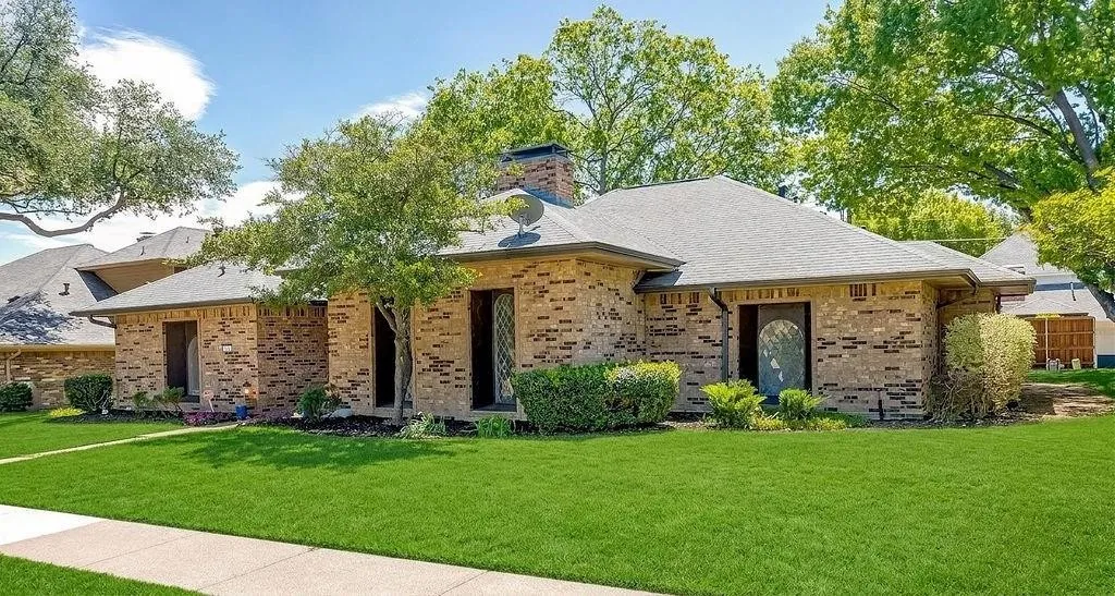 Brick exterior with a dark-pitched roof, showcasing established landscaping and a paved walkway