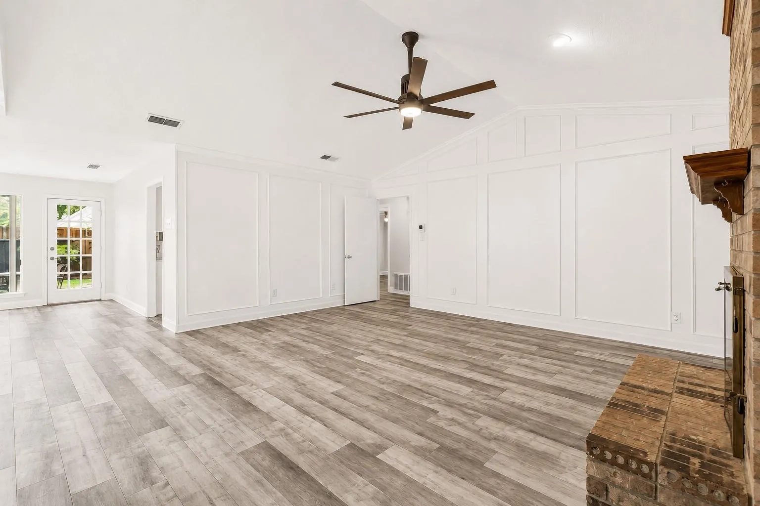 Vaulted ceiling, wood-finish flooring, paneled wall detailing, brick fireplace, and French-style door