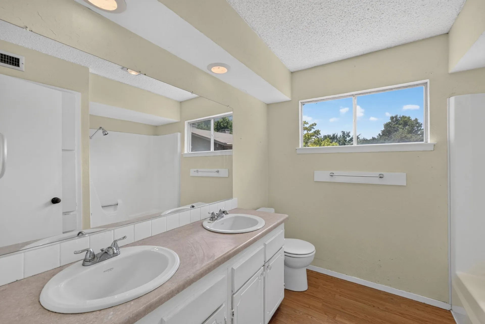 Dual vanity with white cabinetry, wood-finish flooring, and a white shower/tub combination