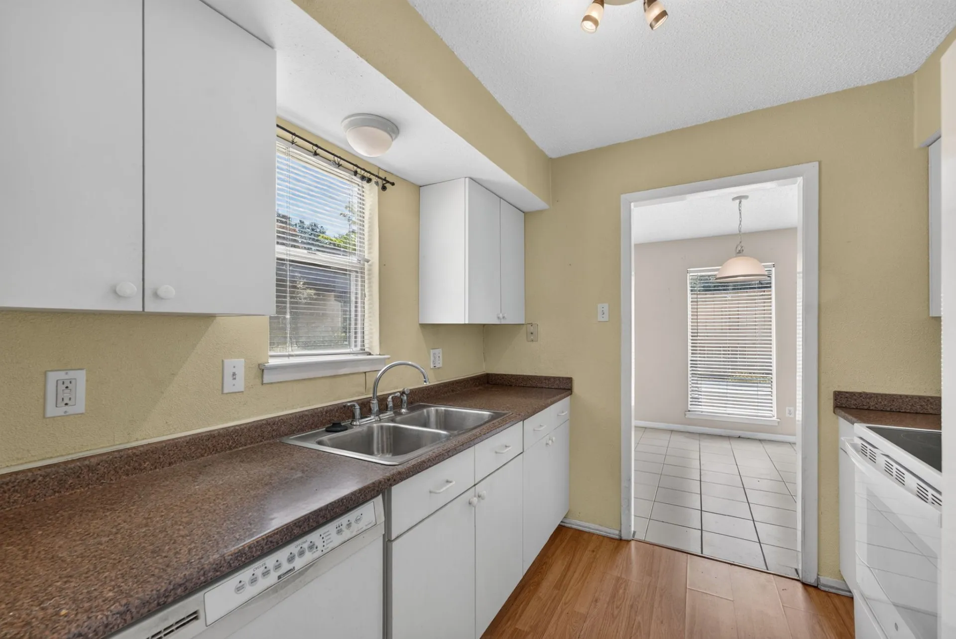 Kitchen featuring white cabinetry, brown countertops, a double-basin stainless steel sink, a built-in dishwasher, and wood-finish flooring
