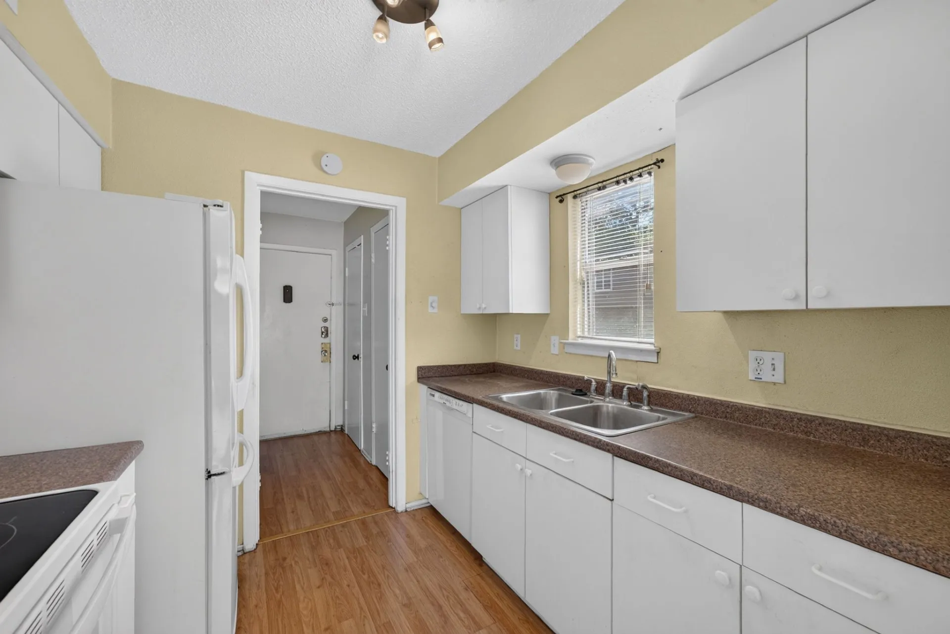 Kitchen featuring white cabinetry, dual-basin stainless steel sink, brown countertops, and wood-finish flooring