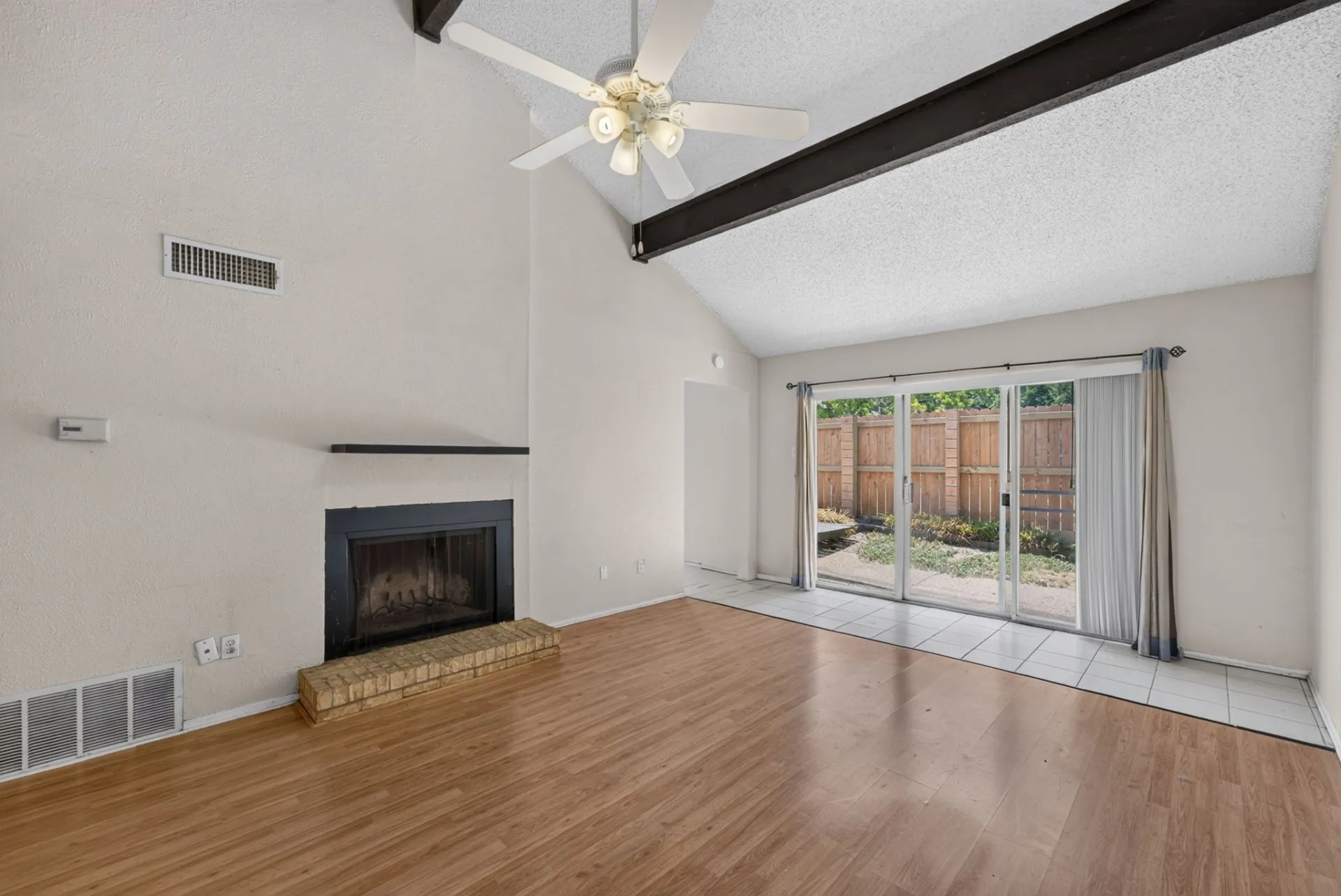 Vaulted ceiling with exposed beams and ceiling fan, wood-finish flooring, fireplace with brick hearth, and sliding glass doors